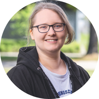 Eine Person mit hellem Haar und Brille trägt eine dunkle Jacke über einem hellen Oberteil.