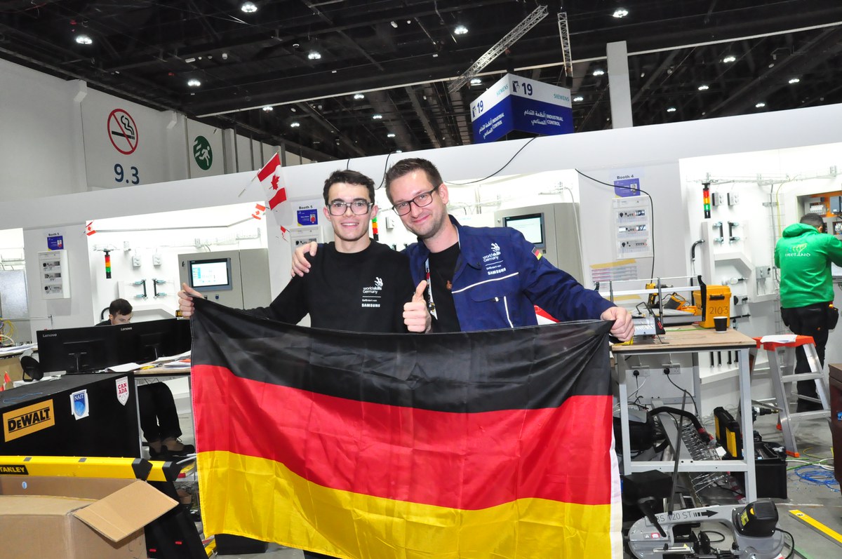 Philipp Winterscheid und Andreas Hochecker mit Deutschlandfahne in Halle vor Computern und Werkbänken.