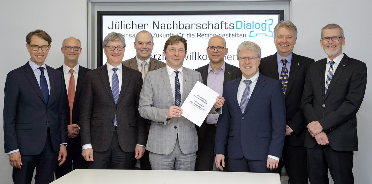 Gruppenbild der Unterzeichner vor einer Wand mit dem Logo des Jülicher Nachbarschaftsdialogs