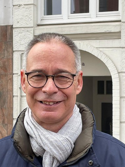 Das Foto zeigt Harald Lange vor einer hellen Gebäudefassade, der direkt in die Kamera lächelt.
