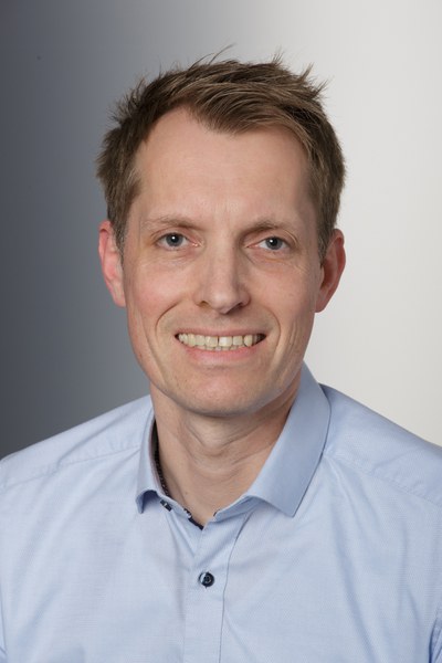 Das Foto zeigt Sven Rank vor einem hellen Hintergrund, der direkt in die Kamera lächelt.