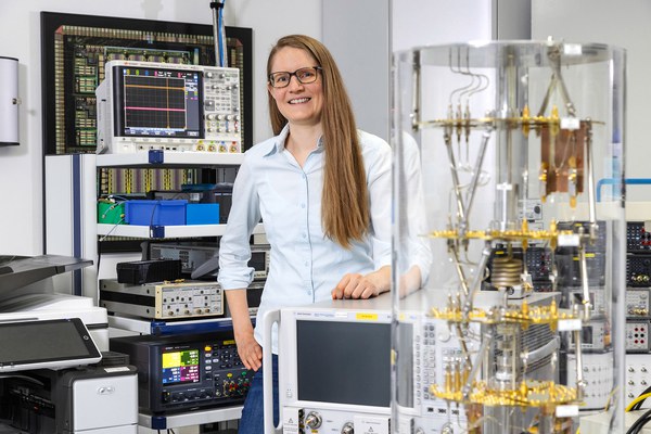 Prof. Lotte Geck steht zwischen technsichen Geräten und lächelt in die Kamera.