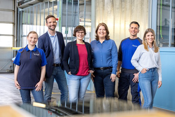 Das Bild zeigt eine Gruppe von Menschen: Zwei Männer und vier Frauen stehen nebeneinander und lächeln in die Kamera. Ihre Kleidung deutet darauf hin, dass es sich um Personen aus der Werkstatt, Administration und dem Wissenschaftsmanagement handelt.