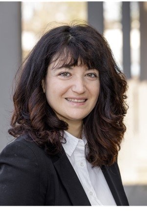 A person with shoulder-length dark curly hair wearing a dark jacket over a light-collapse shirt, smiling slightly. (Mistral: Mistral Medium 3.5, 2026-07-15)