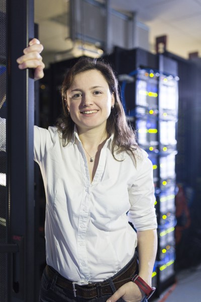 A female scientist leans against the supercomputer structures, smiling.