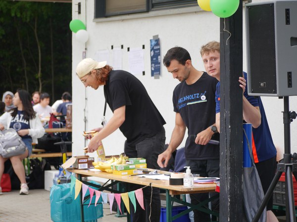 Julian, Johannes and Markus are standing at a stand with snacks. They are at the DocTeam summer party.