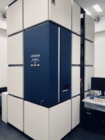 A large, tall, rectangular device with a dark blue panel and white surrounding sections stands in a room with a monitor and a table nearby. (Mistral: Pixtral Large 2411, 2026-03-05)
