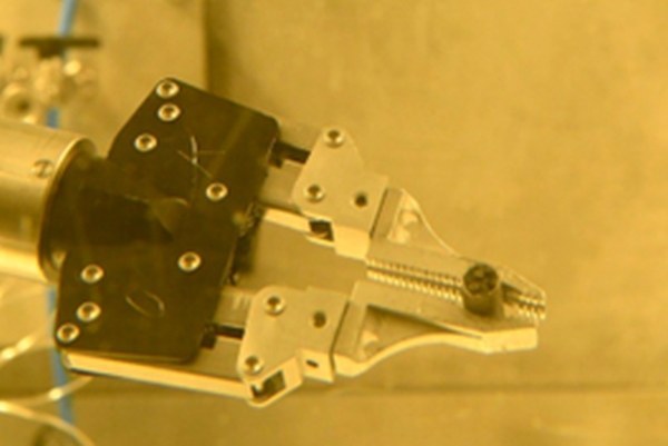 A metallic device with a black component and a silver clamp mechanism attached to a surface. (Mistral: Pixtral Large 2411, 2026-05-12)