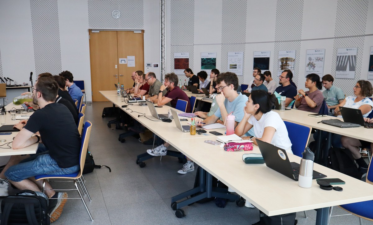 Several people sit at long tables with laptops, notebooks, and beverages in a brightly lit room. (Mistral: Mistral Medium 3.5, 2026-07-27)