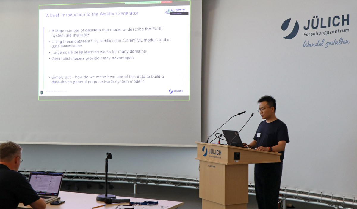 A person stands behind a podium with a laptop, speaking into a microphone, while another person sits at a table with a laptop and microphone in front of a large projection screen. (Mistral: Mistral Medium 3.5, 2026-07-27)