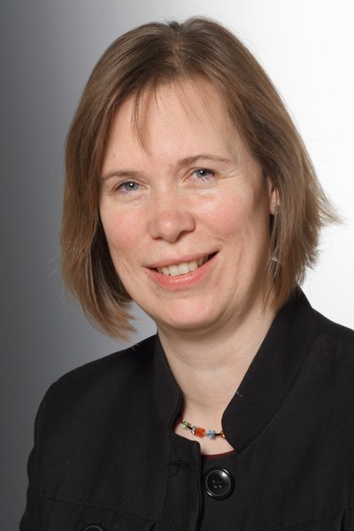 A person with short hair, wearing a dark jacket and a necklace, smiling slightly in front of a plain background. (Mistral: Pixtral Large 2411, 2026-03-17)